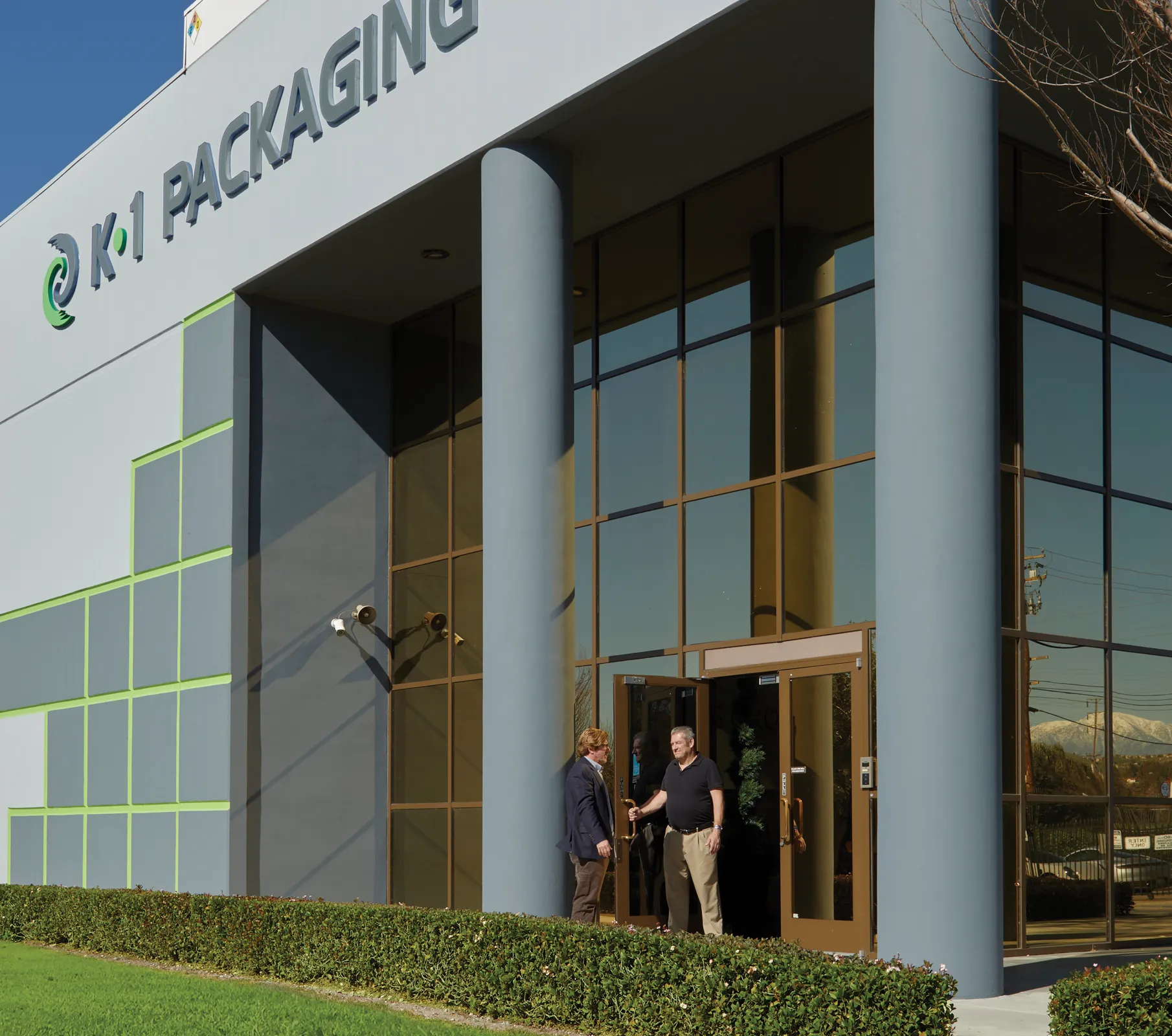 two men standing outside the K1 Packaging building