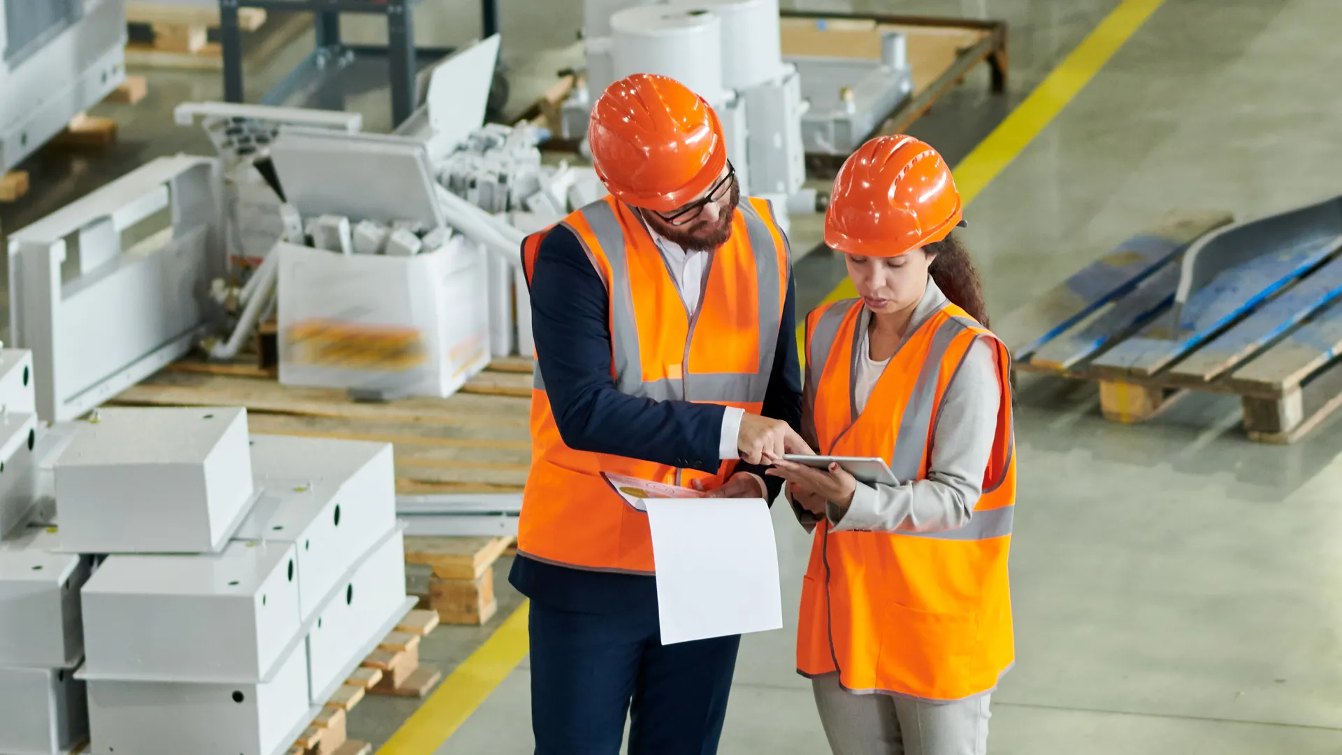 an image two workers in hard hats checking their notes in an industrial setting