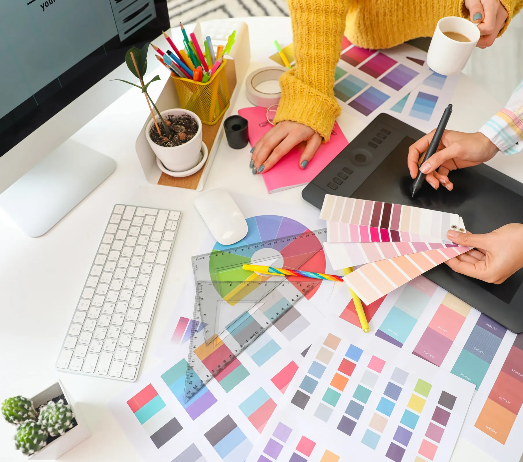 an image of two people standing around a desk, with one of them working a tablet while holding a color picker