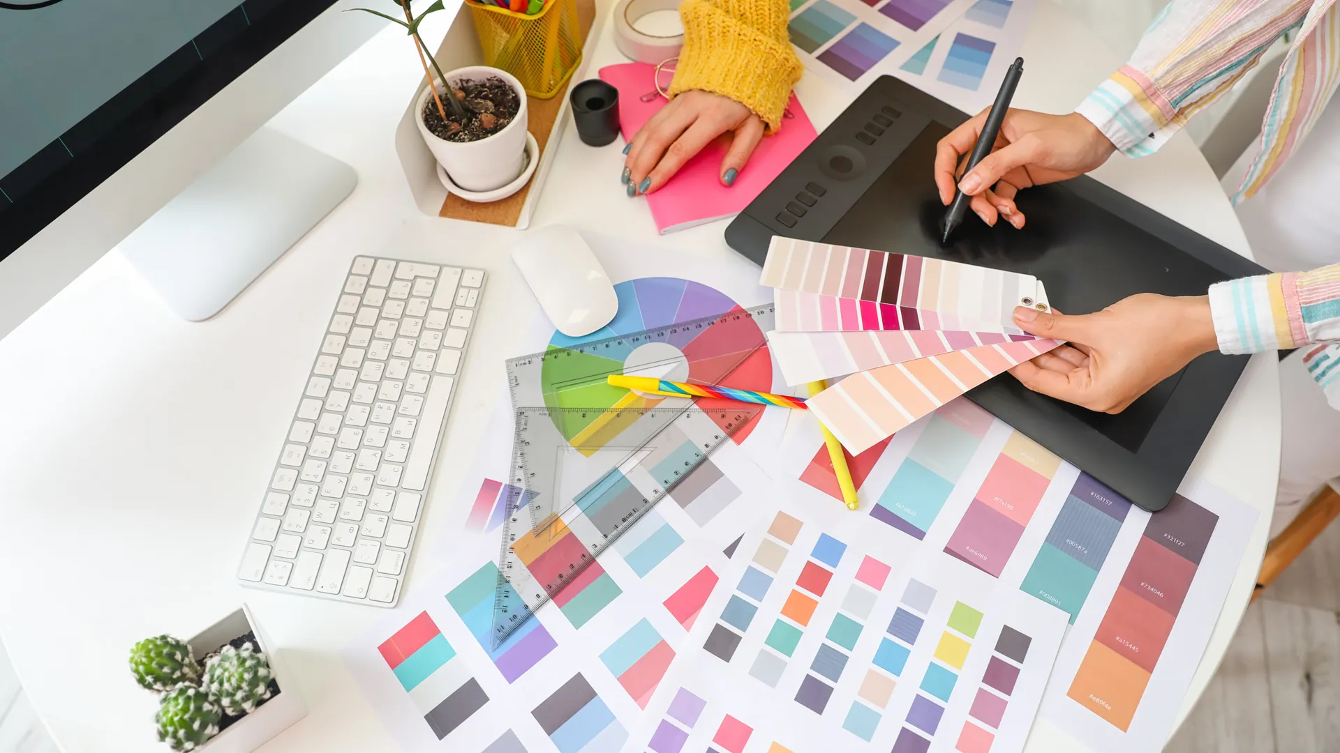 an image of two people standing around a desk, with one of them working a tablet while holding a color picker