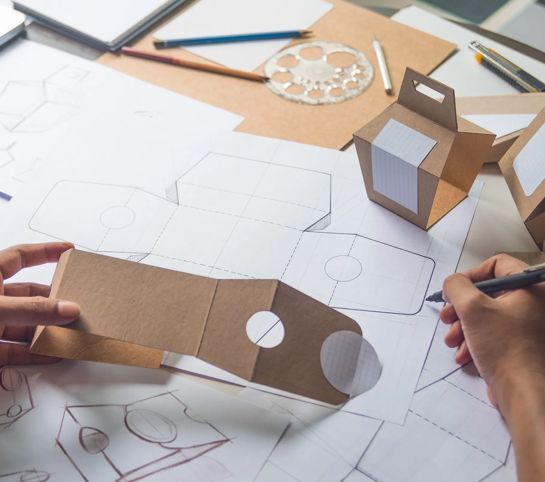 an image of a worker drawing up blueprints while holding a prototype box package