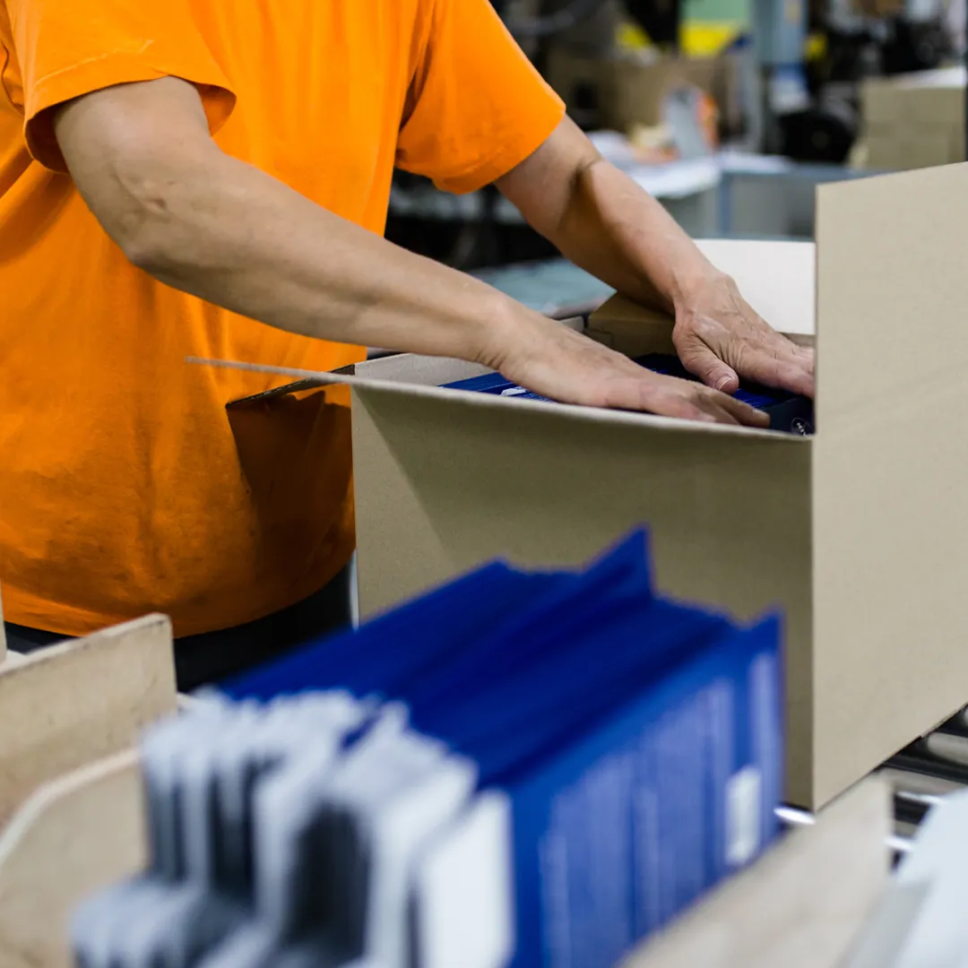 an image of a worker placing products in a cardboard box on a conveyor belt