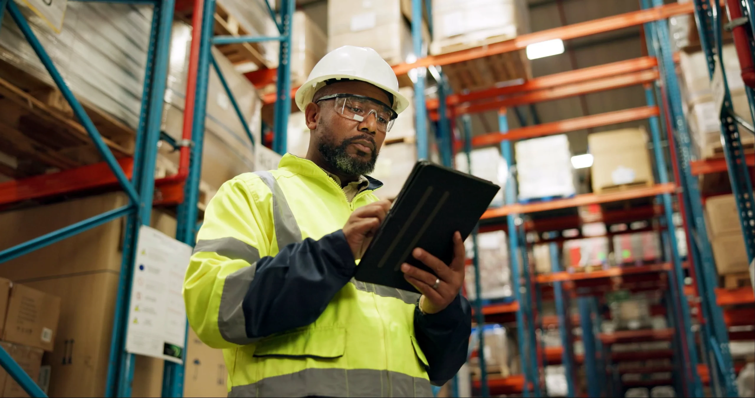 an image of a worker in a hardhat and safety vest checking a tablet in a warehouse setting