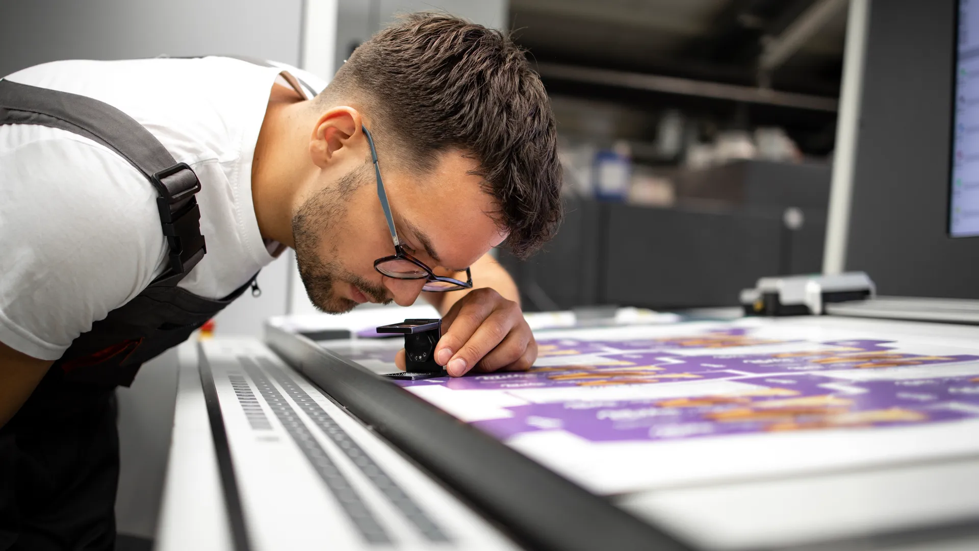 an image of a worker at an industrial workspace using a magnifying glass while looking at blueprints