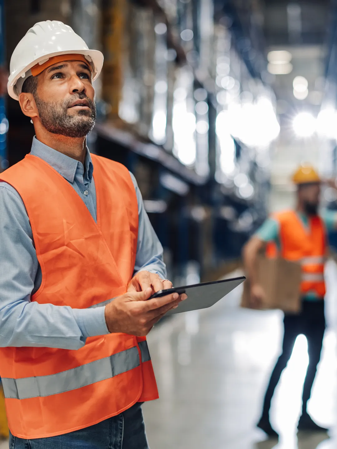 an image of a worker in a hard hat with a tablet looking around in a warehouse setting